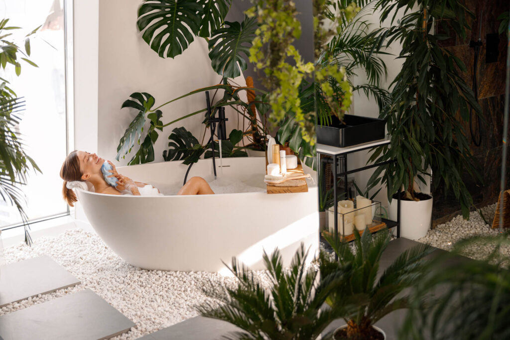 Relaxed young woman bathing in modern bathroom interior decorated with tropical plants - Home remodeling, remodeling contractors chicago