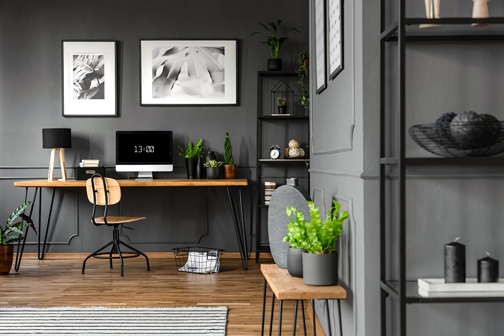 Plants on wooden table in grey home office remodeling with posters above desk with computer monitor